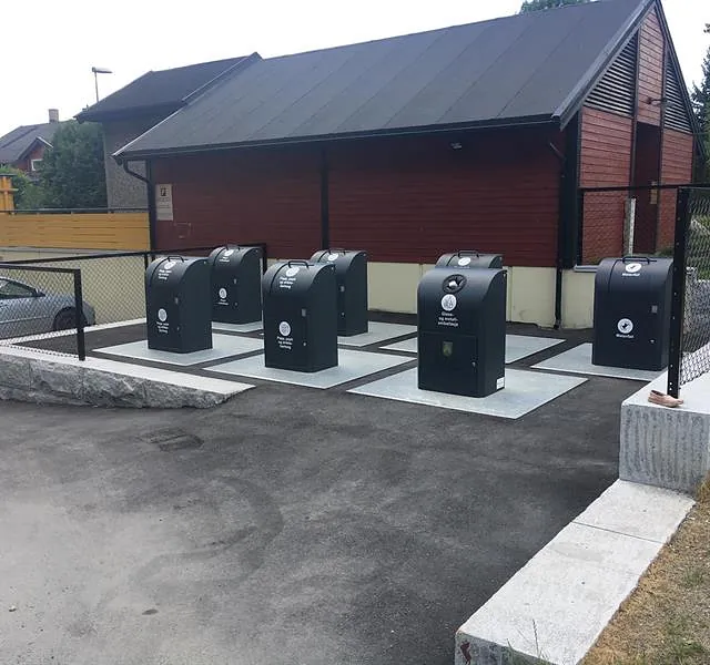 Nedgravd avfallssystem med fire bunntømte beholdere foran boligblokker, klargjort for effektiv kildesortering.