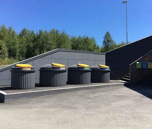 Delvis nedgravde SemiQ beholdere med fargekodede lokk plassert ved moderne boligområde med trapp og postkasser.